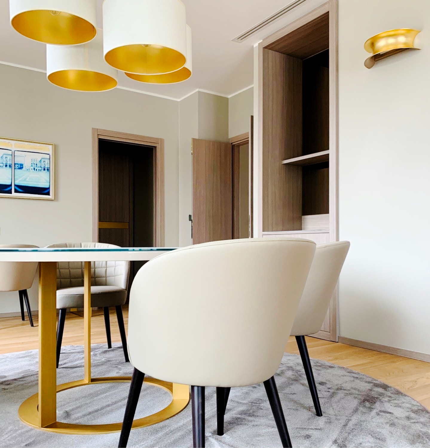 Sala da pranzo con sedie imbottite bianche, tavolo in vetro e lampade dorate